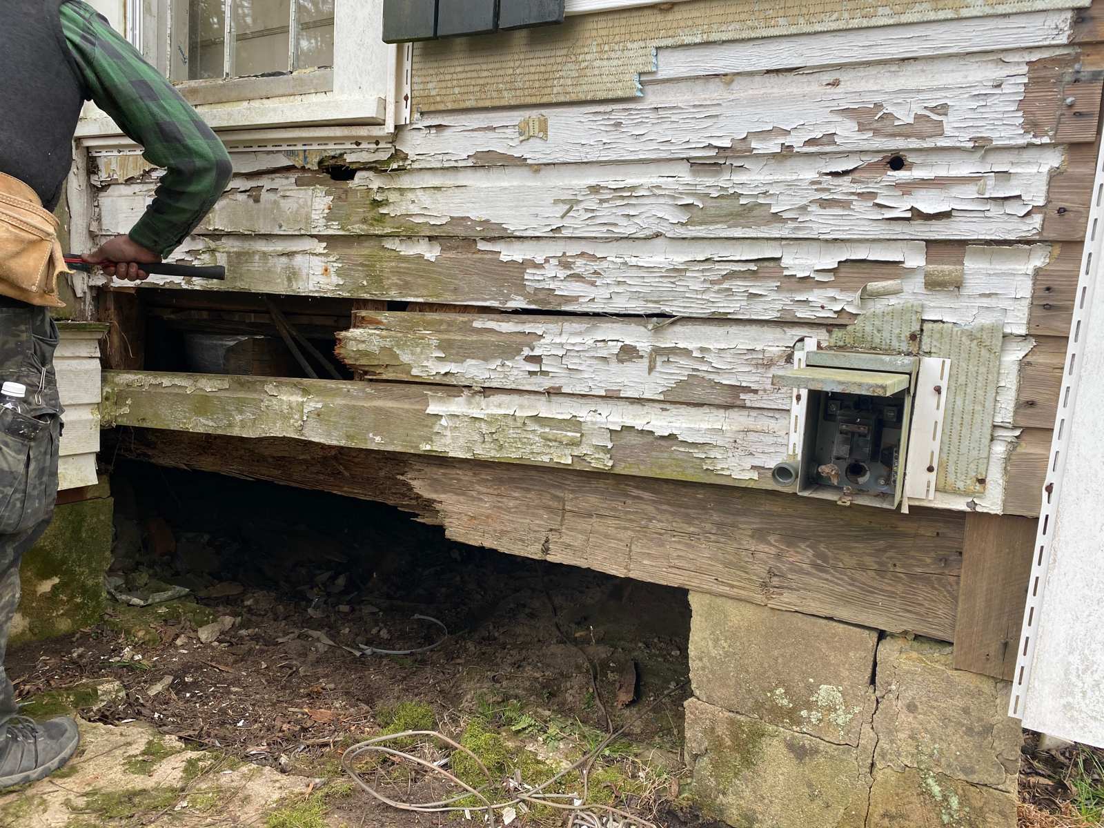The kitchen gable wall: rotted sills, a failed pier, and siding that was mostly paint
