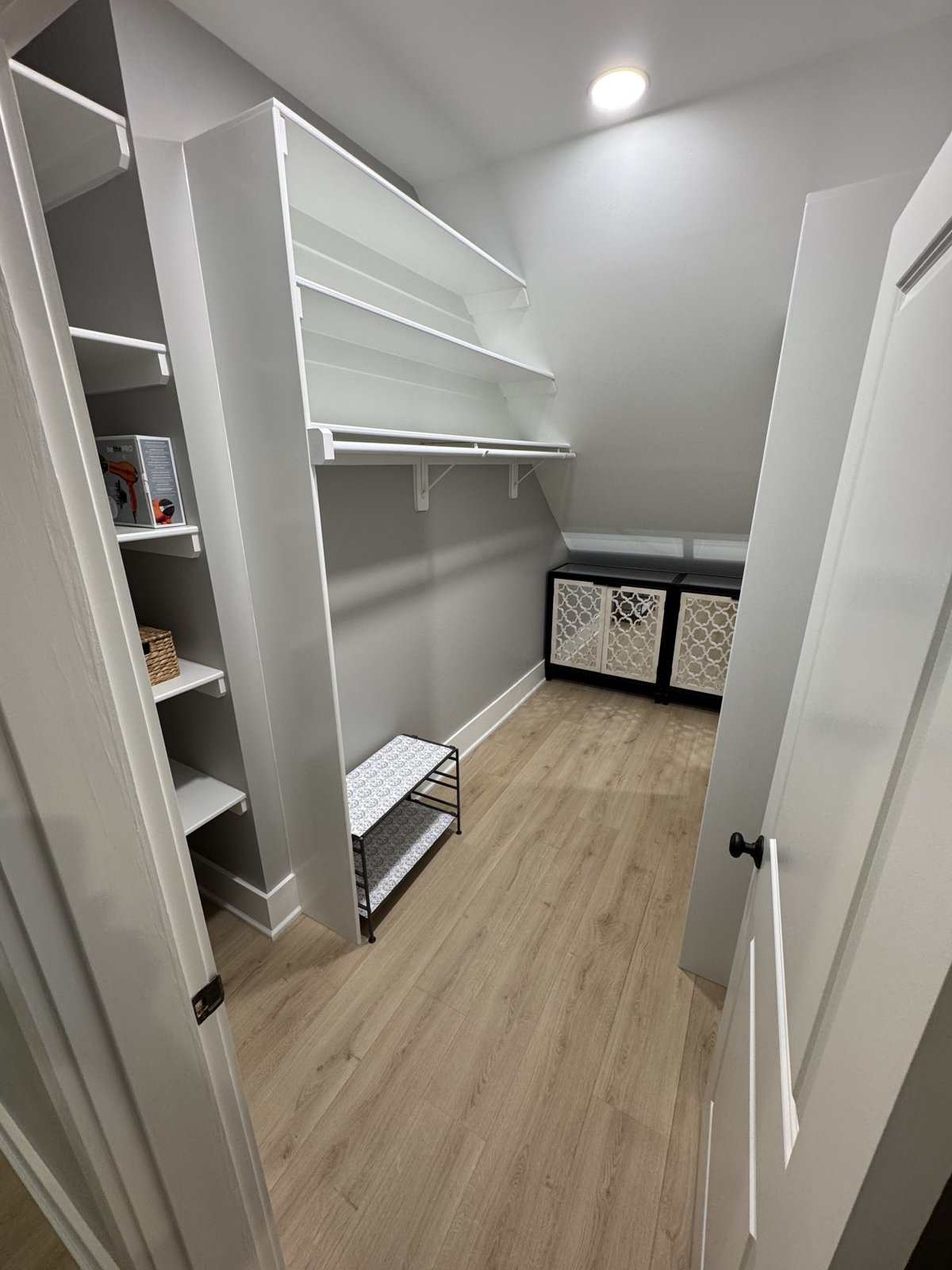 Finished attic closet: painted built-in shelves and hanging rod, matching plank floor, recessed light, and the relocated door