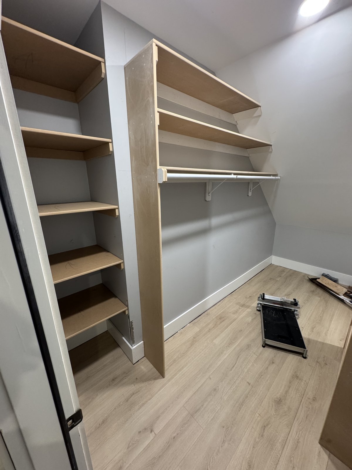 Built-in closet shelving framed from plywood before paint: deep shelves in the nook and a hanging rod with shelves above along the long wall
