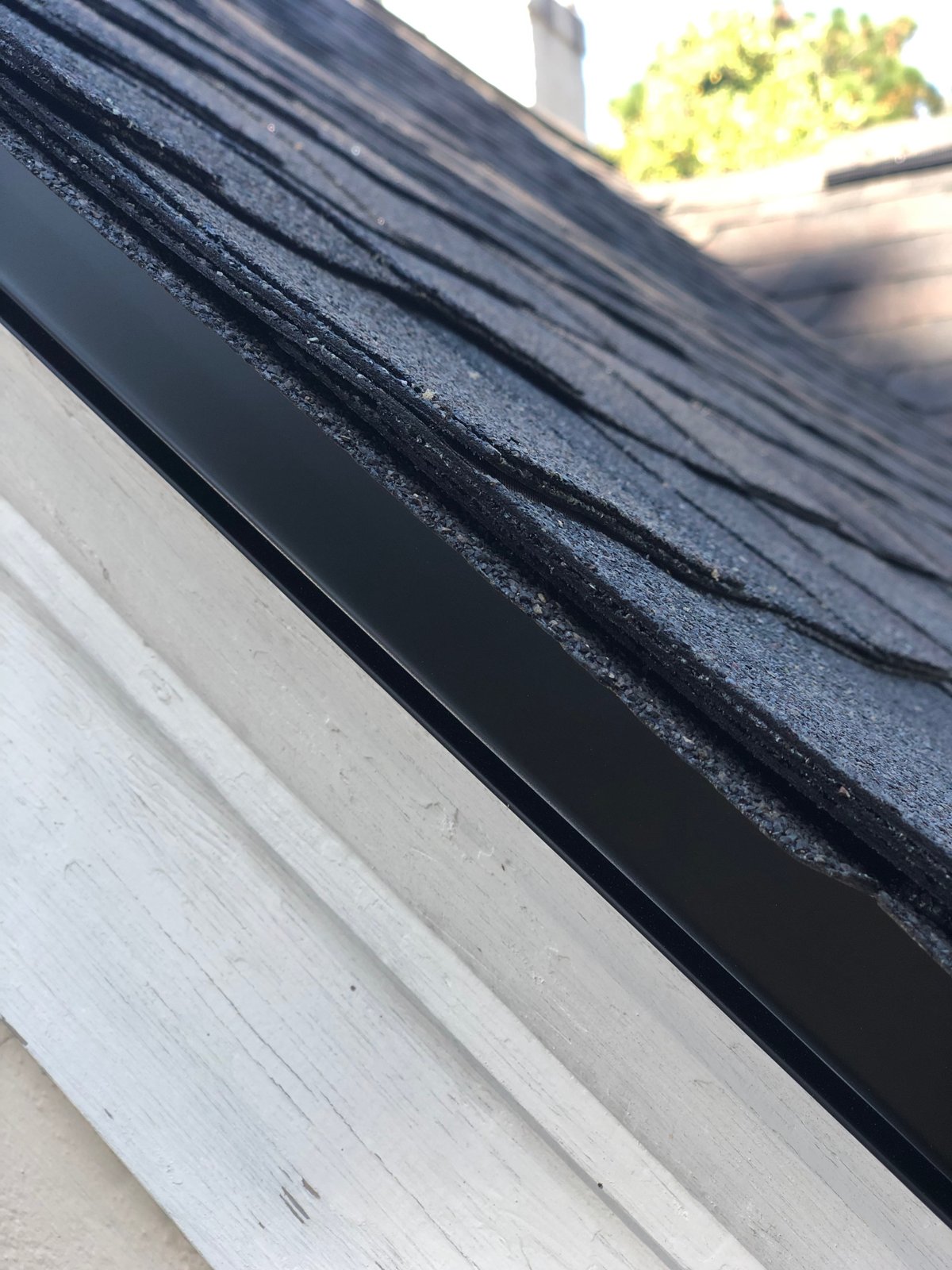 New drip edge and architectural shingles at the roof edge with the chimney behind