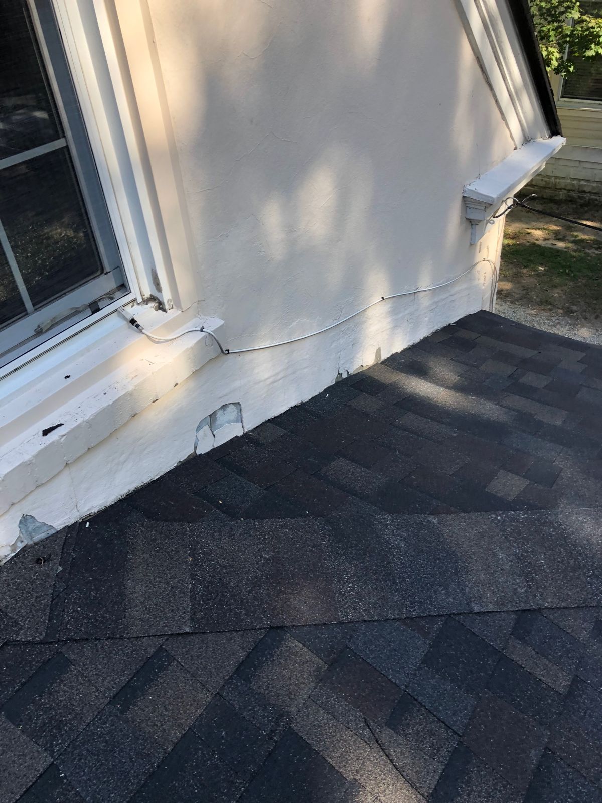 New dark architectural shingles where the lower roof meets the stucco wall and window, flashing complete