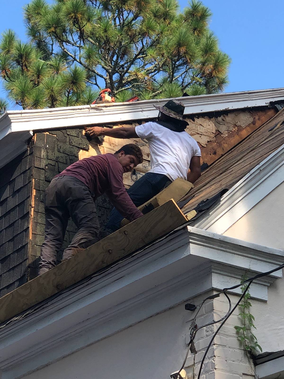 Crew on the roof stripping old cedar shakes off a dormer, exposing dark rotted sheathing beneath